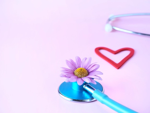 Un corazón rojo y una flor y un estetoscopio sobre un fondo rosa.