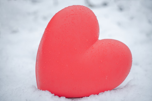 Corazón rojo con gotas de agua sobre la nieve.
