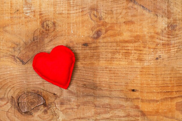 Un corazón rojo hecho con tela sobre una mesa de madera en una vista superior