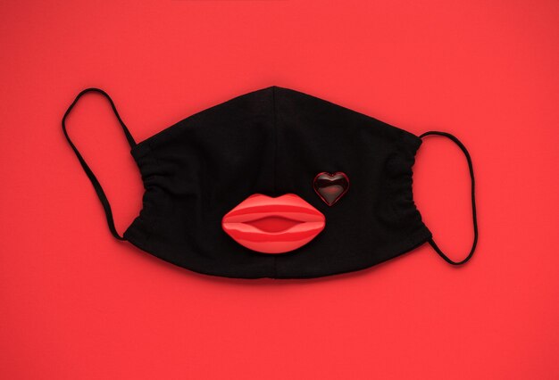 Foto corazón rojo y labios con máscara de protección médica sobre fondo rojo, vista superior, endecha plana. concepto de amor, día de san valentín, salud, protección.