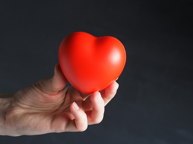 Un corazón rojo en la mano de una mujer sobre un fondo oscuro