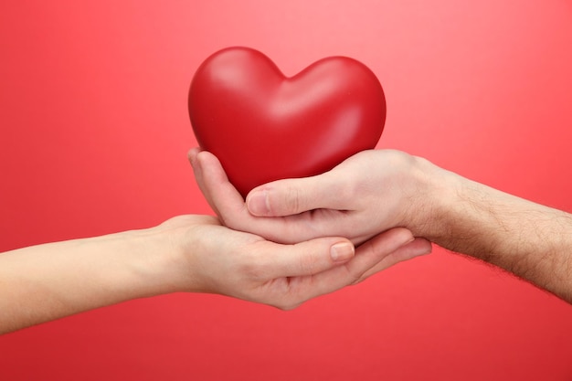 Corazón rojo en manos de mujer y hombre, sobre fondo rojo.