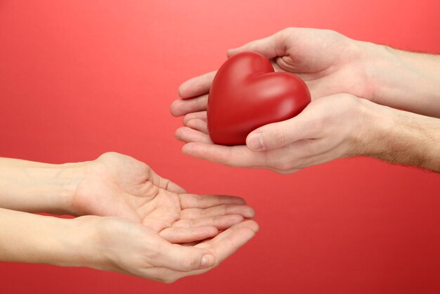 Corazón rojo en manos de mujer y hombre, sobre fondo rojo.