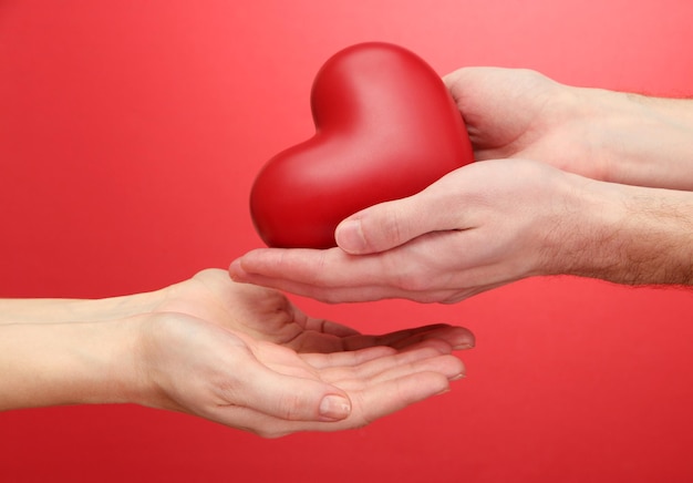 Corazón rojo en manos de mujer y hombre, sobre fondo rojo.