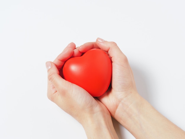 Corazón rojo en manos de mujeres aisladas sobre fondo blanco. Concepto de caridad, salud y amor.