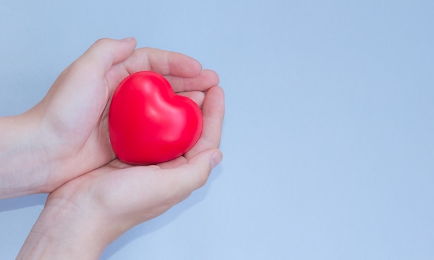 Corazón rojo en manos de niño niño sobre fondo azul.