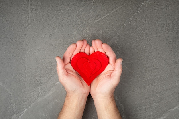Corazón rojo en manos sobre pared gris, el concepto de amor y cuidado de seres queridos y necesitados.