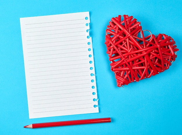 Corazón rojo de mimbre de madera y una hoja blanca vacía de bloc de notas