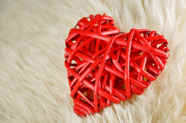 Un corazón rojo de mimbre yace sobre nosotros en una manta de lana blanca, concepto de San Valentín
