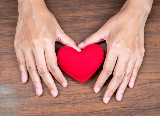 Corazón rojo en primer plano de las manos sobre fondo de madera