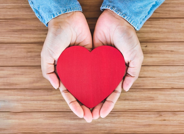 Corazón rojo en primer plano de las manos sobre fondo de madera