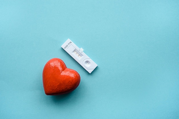 Un corazón rojo y una prueba de coronavirus en un fondo azul.