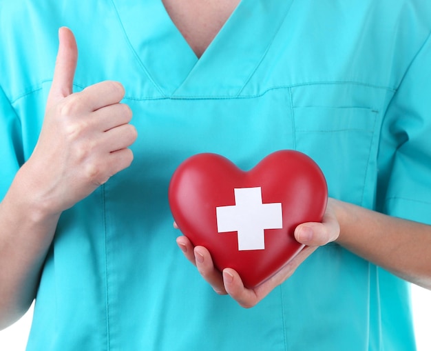 Foto corazón rojo con signo de cruz en primer plano de la mano del médico aislado en blanco