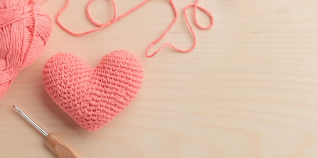 Corazón rosa amigurumi de ganchillo con ganchillo y un hilo sobre un fondo de madera Banner del día de San Valentín