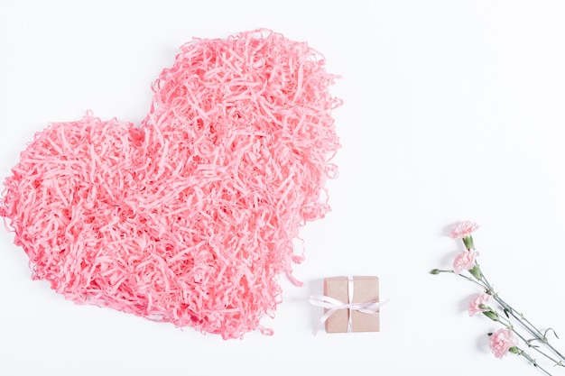 Corazón rosa decorativo, caja pequeña con un regalo y cinta y flores sobre una superficie blanca