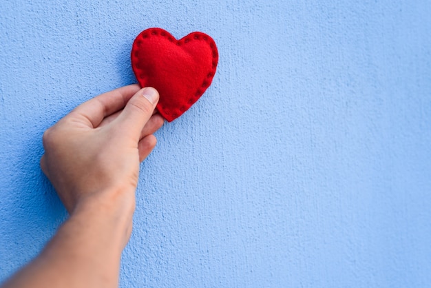 Corazón de San Valentín rojo en la mano de un chico sobre un fondo azul.