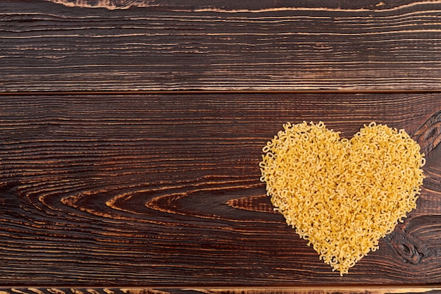 Corazón stelline de macarrones, vista superior. Corazón de alimentos crudos sobre fondo de madera, espacio de copia. Decoración del día de San Valentín.