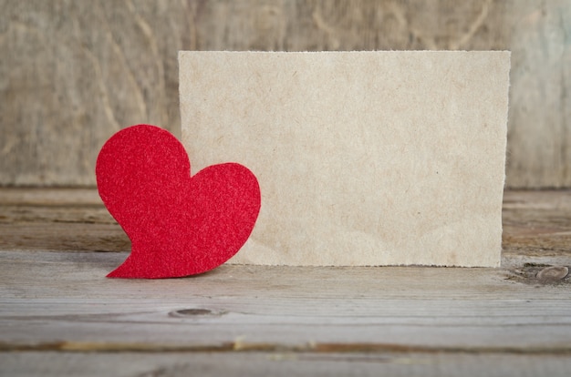 Corazón de tela roja con hoja de papel de pie sobre una tabla de madera en la mesa de madera