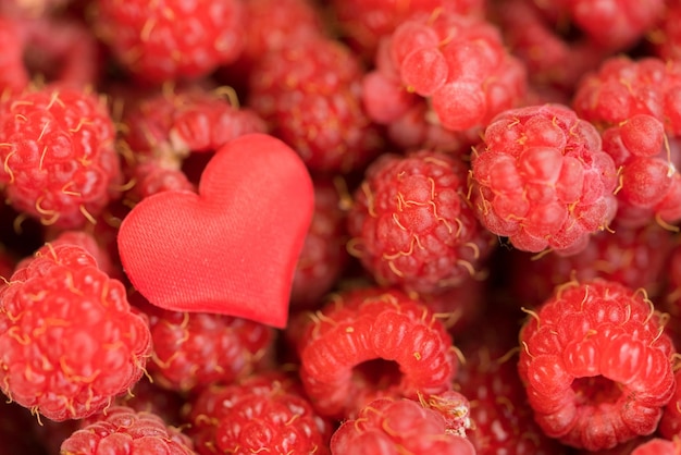 Corazón textil rojo sobre el fondo de frambuesas maduras