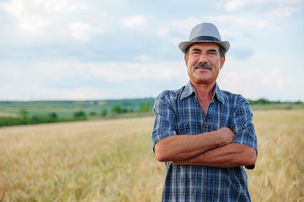 En el corazón de las tierras de cultivo un sabio y anciano granjero con las manos cruzadas posa orgullosamente en el