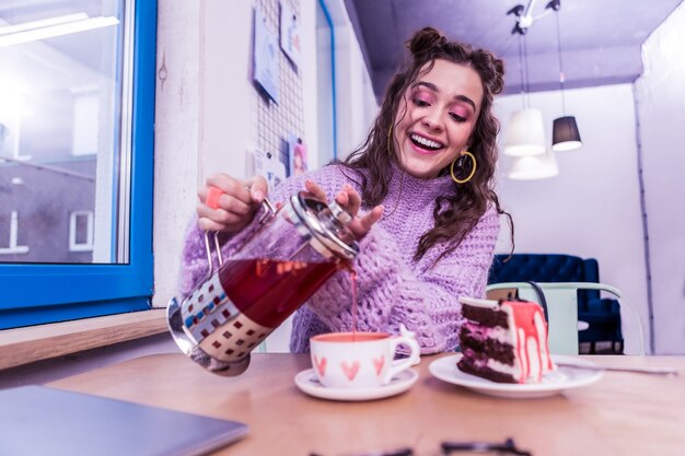 Corazones de acuarela. Riendo señora positiva vertiendo té caliente en taza bonita mientras está sentado en la mesa