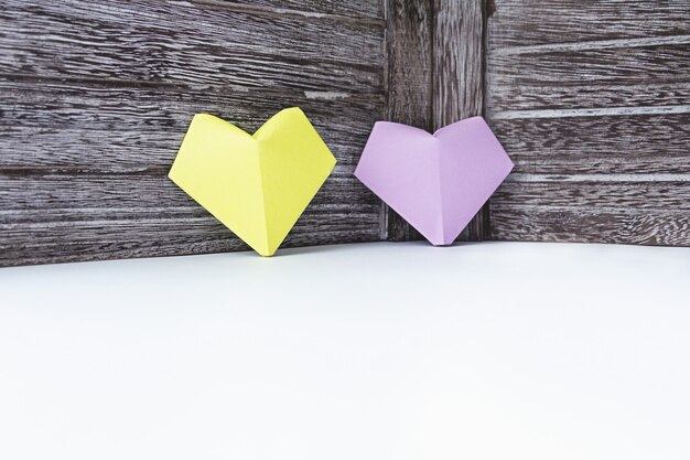 Los corazones de color lila y amarillo del papel están en el fondo de una tabla de madera oscura