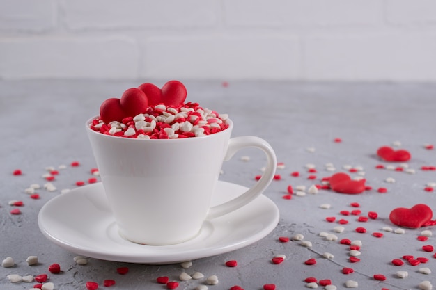 Corazones dulces rojos del caramelo de azúcar en una taza de café. Decoración de concepto de amor y día de San Valentín.
