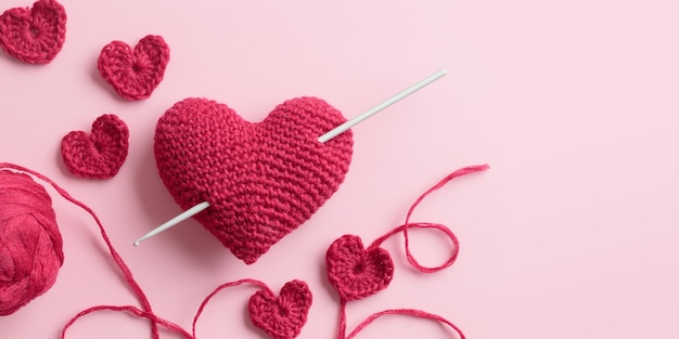 Corazones de ganchillo amigurumi rojo púrpura burdeos con gancho de ganchillo sobre un fondo rosa Banner de San Valentín