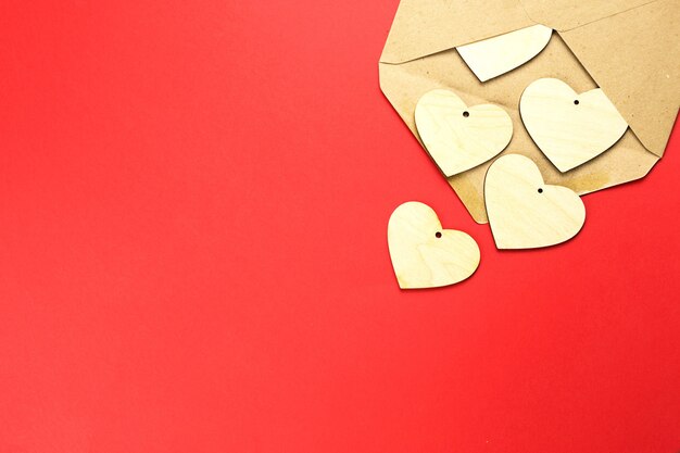 Los corazones de madera se derraman de un sobre abierto sobre un fondo rojo.