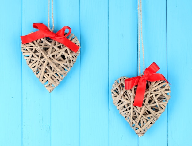 Corazones de mimbre con lazo rojo sobre fondo de madera