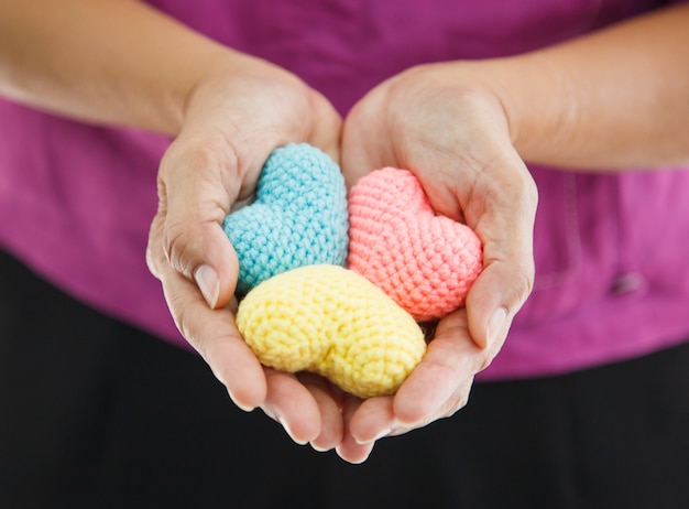 Corazones multicolores de colores en manos de las mujeres, representando una mano amiga