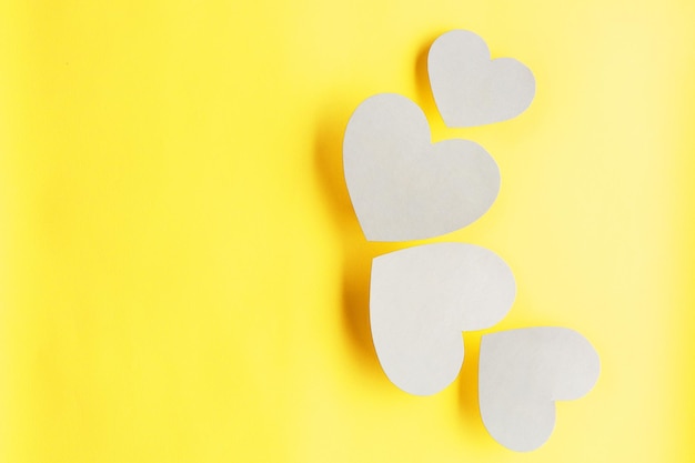 Corazones de papel blanco sobre fondo amarillo claro