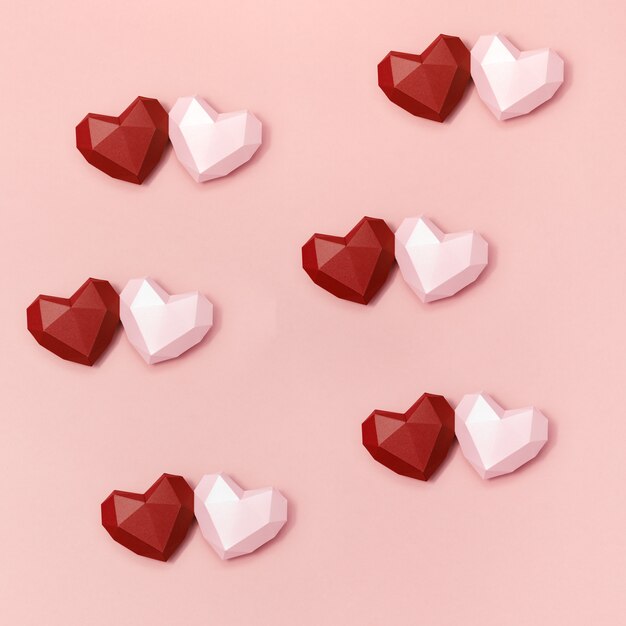 Corazones de papel poligonal rojo y rosa juntos en superficie color crema. Fondo de vacaciones con espacio de copia para el día de San Valentín.