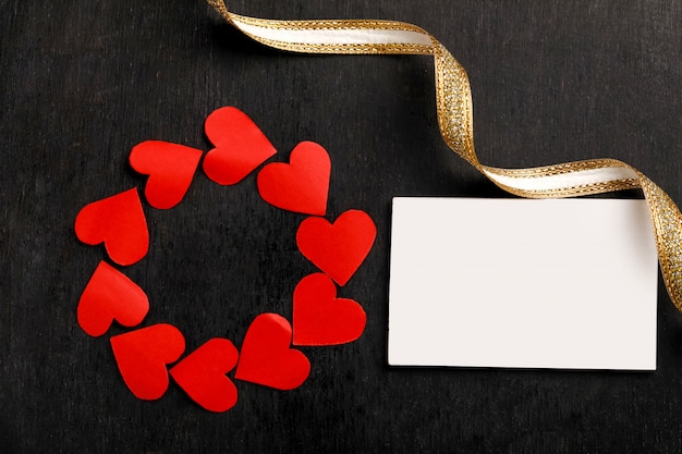 Corazones de papel rojo, cinta dorada y tarjeta en blanco