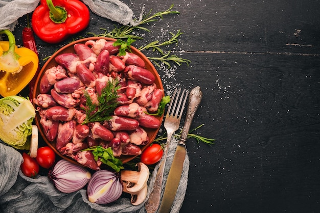 Corazones de pollo crudo en el plato listo para cocinar con romero y especias sobre un fondo de madera negra Vista superior Espacio libre para texto