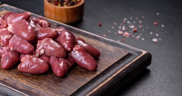 Corazones de pollo crudos sin cocer en una tabla de cortar de madera sobre una mesa de hormigón oscuro