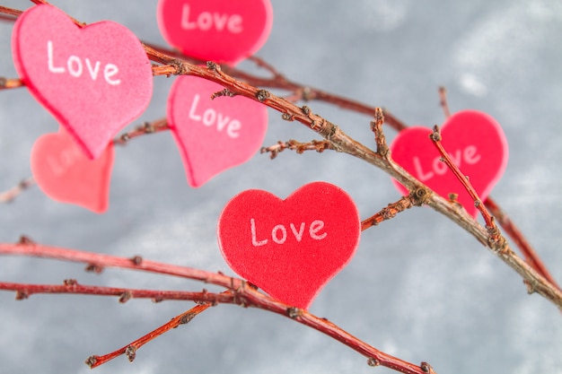 Los corazones rojos aman la caída en ramas en fondo concreto. Árbol de amor