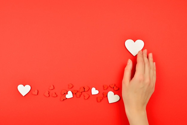 Corazones rojos y blancos sobre un fondo rojo. Mujer sosteniendo corazón blanco. Copie el espacio.