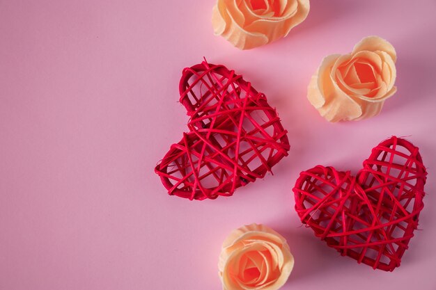 Corazones rojos y capullos de rosa naranjas sobre un fondo rosa. Concepto para el día de San Valentín. Lugar para el texto.