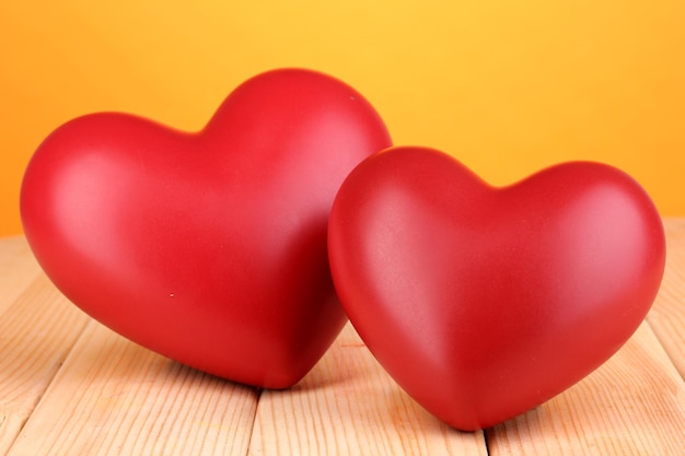 Corazones rojos decorativos en la mesa de madera sobre fondo naranja