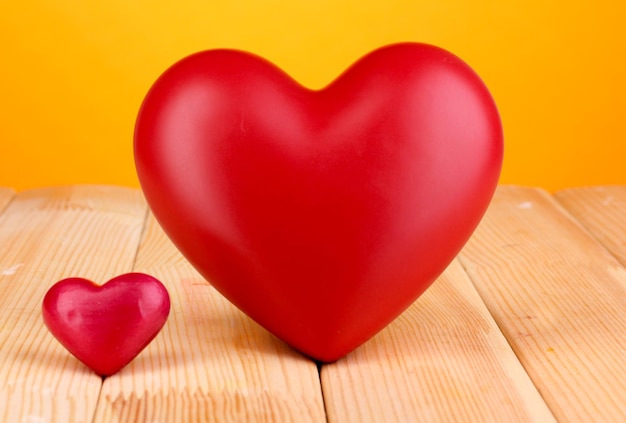 Corazones rojos decorativos en la mesa de madera sobre fondo naranja