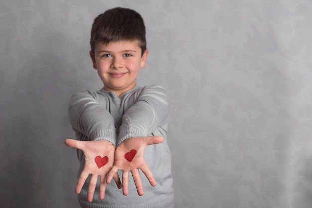 Foto corazones rojos en las palmas del bebé. el dibujo en rojo en los brazos del niño es un primer plano. bebé sobre un fondo gris muestra palmas con un patrón de corazones