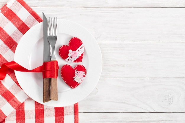 Corazones de tela hechos a mano de San Valentín en un plato para una cena romántica con fondo de espacio de copia sobre una mesa de madera blanca