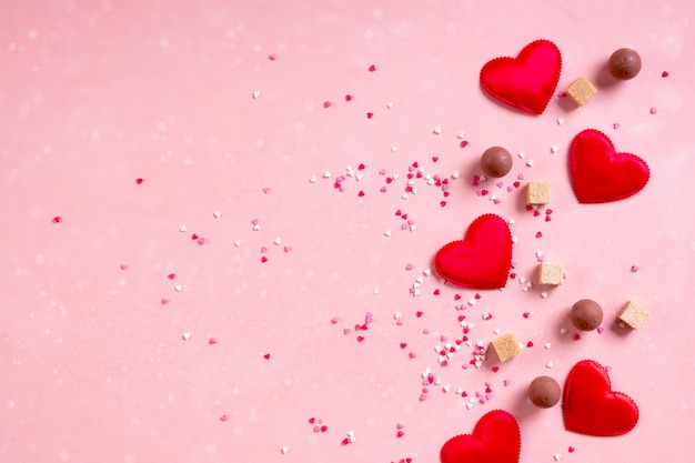 Corazones de tela roja, terrones de azúcar, confeti, dulces dulces de chocolate sobre fondo rosa. Día de San Valentín 14 de febrero amor concepto mínimo. Lay Flat, espacio de copia, espacio para texto, banner