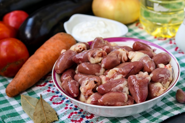 Corazones y vegetales crudos de pollo: zanahorias, berenjenas, tomates y cebollas, para una cena sabrosa y saludable, orientación horizontal