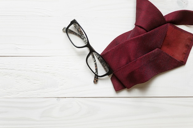 Corbata masculina y anteojos acostado sobre fondo blanco de madera