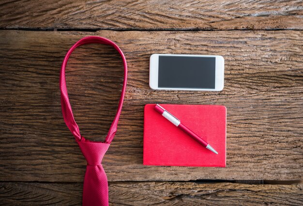 Corbata roja, bolígrafo, cuaderno, teléfono inteligente en mesa de madera