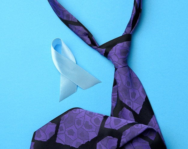 Corbata de seda púrpura para hombre y cinta azul doblada en un lazo sobre fondo azul, símbolo de la lucha y el tratamiento del cáncer de próstata, espacio de copia