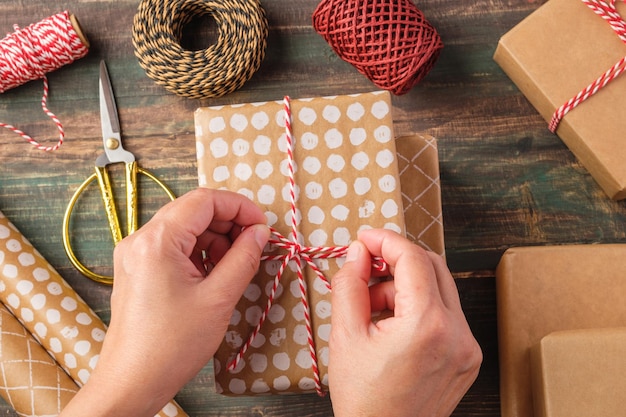 Corda amarrada à mão na caixa de presente de Natal com decoração de papel pardo e pinheiro na mesa de madeira