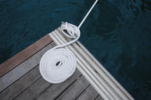 Foto corda de barco branca presa a uma doca de madeira com água escura abaixo